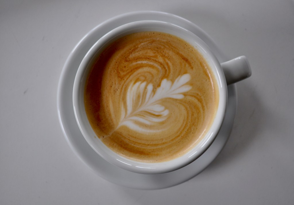 An image showing a simple example of latte art: a geometric design made by pouring steamed milk into an espresso base inside a large coffee cup.