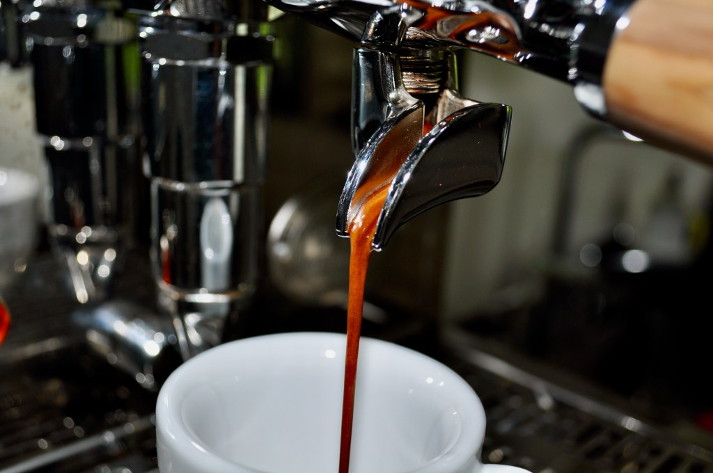 The image shows an espresso drink pouring from the spout of a portafiler.