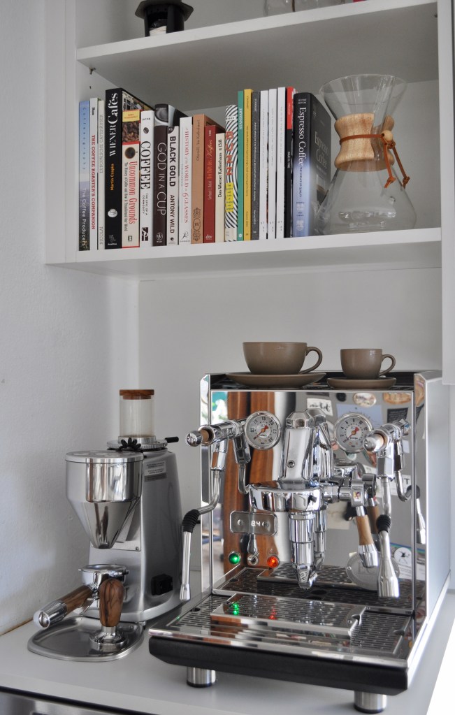 An image of my current coffee corner: with a ECM Synchronika dual-boiler espresso machine, along with a Mazzer Mini grinder, one espresso cup and saucer, one cappuccino cup and saucer, along with a Chemex brewer and range of books about various aspects of coffee.